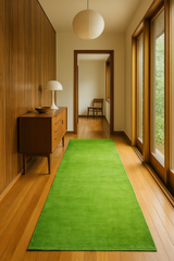 Green runner rug on a wooden floor with a wooden cabinet and lamp in a room with large windows.