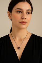 Woman wearing a necklace with a purple gemstone against a neutral background